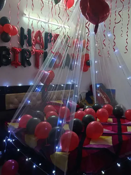 A red and black themed canopy decoration for a birthday. The fairy lights and balloons on the bed create an intimate and celebratory setting.