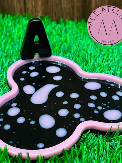 A personalized coaster with the initial 'A' in a fun black and pink bubble design, perfect for your bedside bottle.