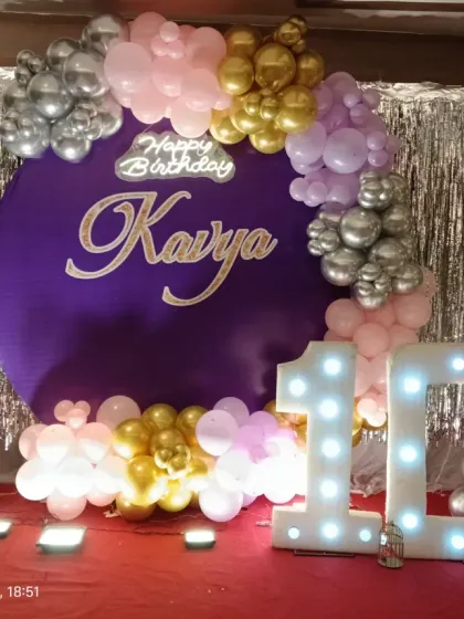 A stylish 10th birthday party with a purple, pink, and silver theme. The decor features a silver shimmer backdrop, a custom name cutout, a balloon garland, and a large "10" marquee number.