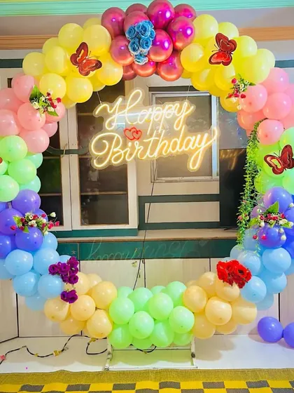 A full-circle rainbow balloon arch with a 'Happy Birthday' neon sign. This vibrant and colorful setup is perfect for creating a cheerful and festive party atmosphere.