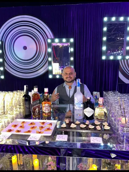 Our founder Sid behind a sleek, modern bar at a private party. The setup includes a mirrored bar front, vanity lights, and a tray of our signature edible cocktails.