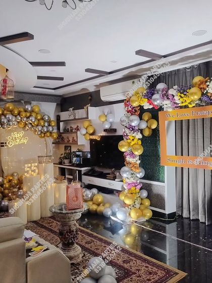 A lavish 55th birthday party at home, with a gold and silver balloon backdrop and a separate photo frame arch.