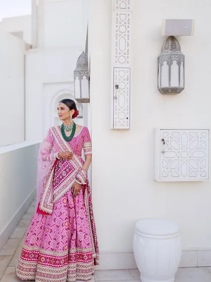 The full view of this traditional yet modern look. The makeup is flawless and radiant, complementing her beautiful pink bandhani lehenga perfectly.