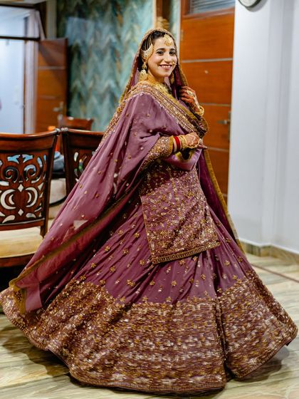 A full-length portrait of a bride in a stunning purple lehenga, capturing the flow and grandeur of her wedding outfit.