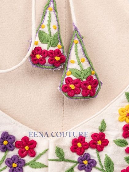 A garden of flowers on a blouse. This white raw silk piece is covered in vibrant, multi-colored floral French knot embroidery, making it a cheerful and eye-catching addition to any festive wardrobe.