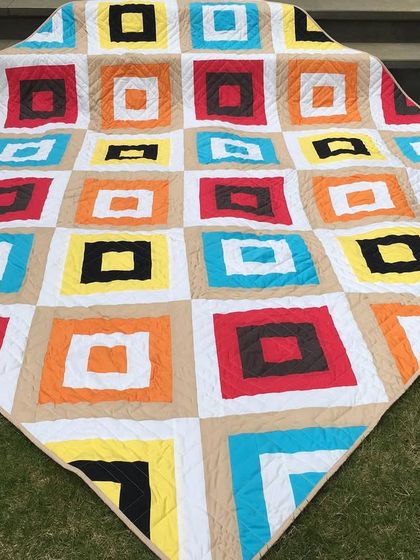 A colorful, modern quilt with a "square in a square" pattern, displayed outdoors.