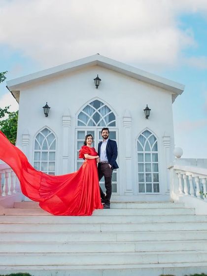 A beautiful, wide shot of a couple on the steps of a white chapel set, with a flowing red dress adding a dramatic and romantic element.