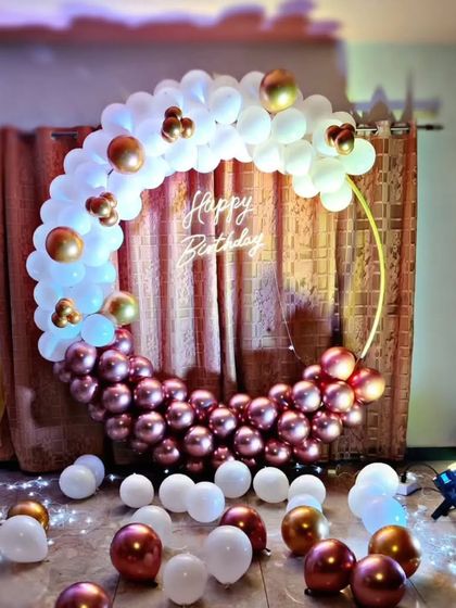 A half-ring of white and rose gold balloons with a neon sign, creating a simple yet beautiful photo spot at home.