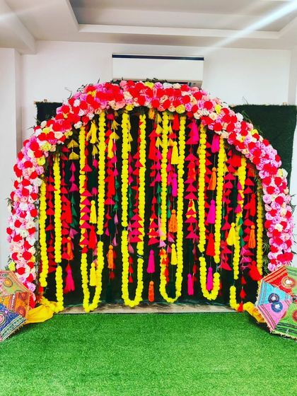 A stunning Mehendi photo booth with a lush green carpet, a floral arch, and hanging marigold garlands.