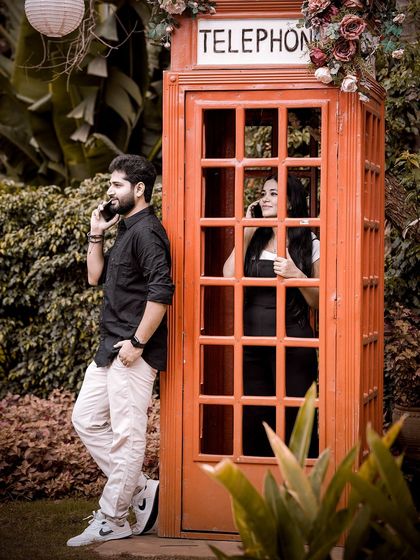 A playful pre-wedding photo featuring a classic red telephone booth, with the couple pretending to be on a call, adding a touch of British vintage charm.