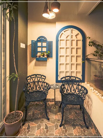 A charming balcony nook with blue and white decorative window frames and cast iron chairs, creating a Mediterranean-inspired feel.