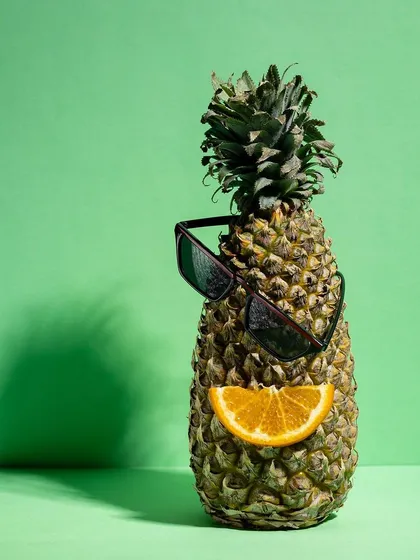 Another whimsical product shot, creating a "face" on a pineapple using sunglasses and an orange slice. This type of creative still life is memorable and highly shareable.
