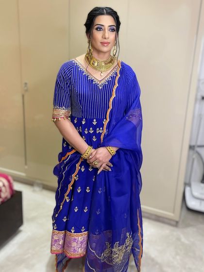 The full view of this coordinated look. The bold eye makeup stands out beautifully against the rich blue of her traditional suit.