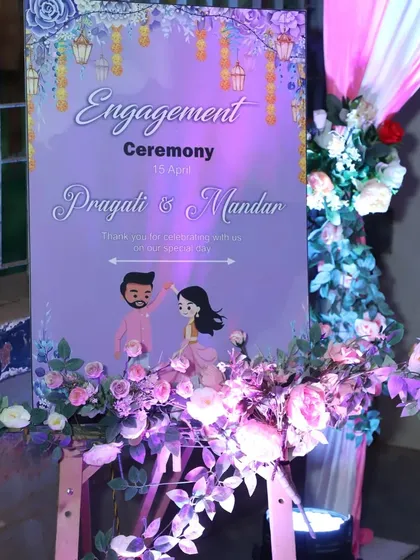 A close-up of a personalized welcome stand for Pragati and Mandar's engagement ceremony, featuring a cute cartoon illustration.