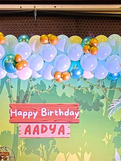 A close-up of a jungle-themed backdrop with a custom 'Happy Birthday' sign. The balloon garland on top adds a pop of color.