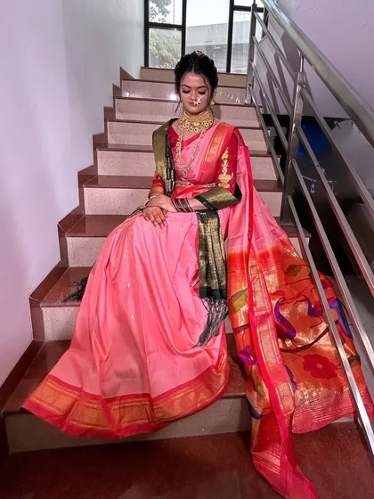A complete bridal look featuring a gorgeous pink `Paithani` saree. The makeup is designed to complement the rich colors of the outfit while keeping the skin looking fresh and dewy.
