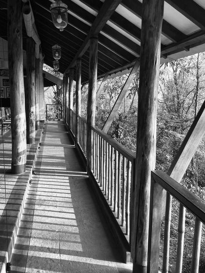 A black and white photo of the yoga pavilion's veranda at PLENTI House, showing the beautiful play of light and shadow created by the wooden structure.