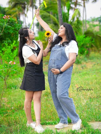 A fun and playful outdoor shot with friends. The mother-to-be is wearing casual denim overalls and sharing a laugh.
