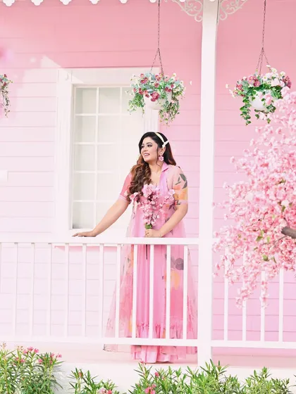 The model poses on the porch of a pink house, surrounded by flowers. This shot has a charming, storybook quality that is both sweet and fashionable.