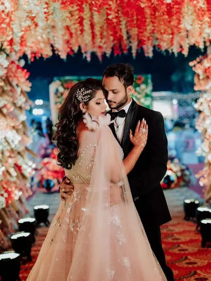A fairytale wedding moment. The bride and groom are framed by a beautiful floral arch, and her makeup looks flawless even from a distance.