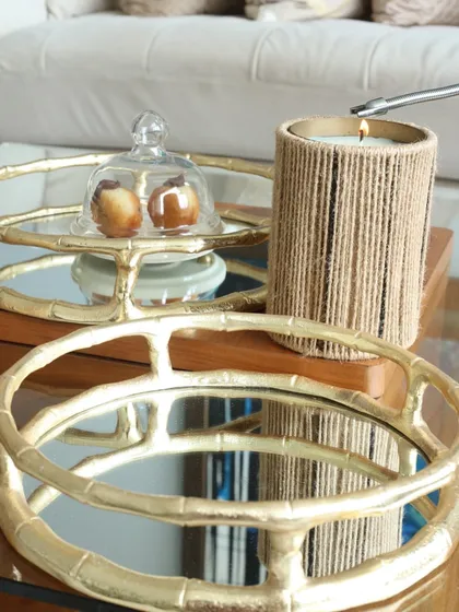 Our round bamboo-style mirror tray, styled with a cloche and a candle. The mirrored surface beautifully reflects light, creating a warm and inviting atmosphere.