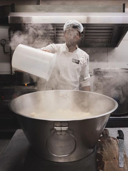 A chef adds hot water to the cheese curds, a critical step that allows the curds to melt and stretch into mozzarella.