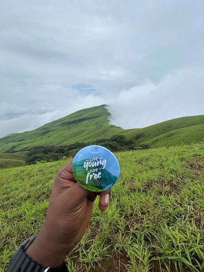 Holding up our "Live Young, Live Free" badge against the backdrop of Netravathi peak.