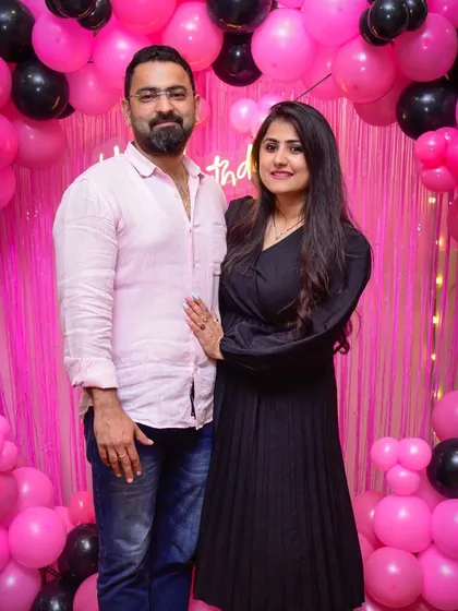A lovely couple posing in front of a pink and black balloon wall, celebrating a special day.