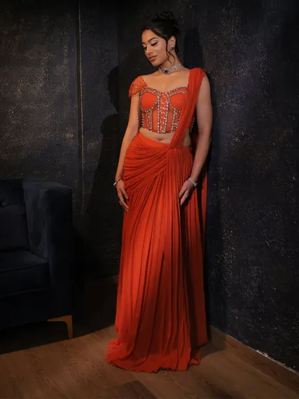 A relaxed pose in the orange corset saree, showing its versatility and modern appeal for any celebratory event.