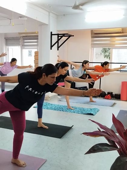 An instructor guides the class through Virabhadrasana III (Warrior III), emphasizing balance and extension.