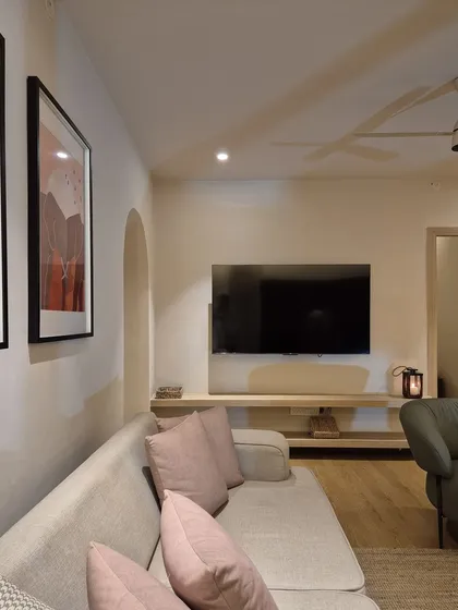 The living area in our Coorg homestay project features soft, earthy tones and natural textures. An arched niche and a simple wooden media console create a minimalist yet warm focal point, perfect for a relaxing evening.