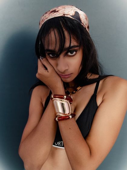 An edgier take on accessory photography. The model's pose is dynamic and her gaze is intense. The lighting is focused to pick up the details of the chunky bracelets and the pattern on the headscarf, creating a strong, fashion-forward look.