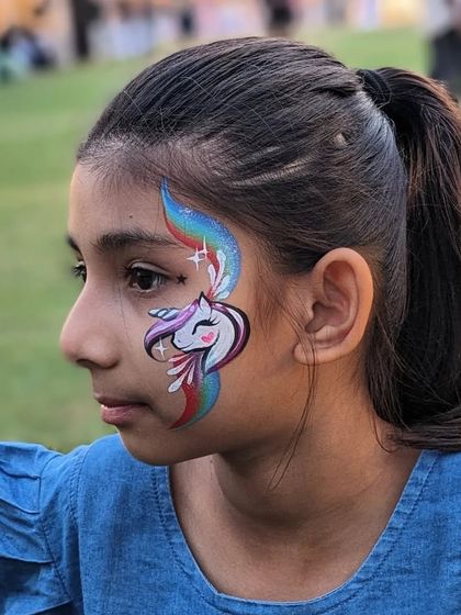 A smiling girl with a rainbow unicorn face paint. This design is always a favorite at parties and events.