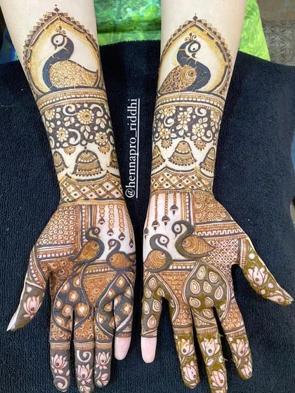 This design is filled with classic motifs. It features majestic peacocks on both the palms and forearms, complemented by delicate hanging jhumka (earring) elements.
