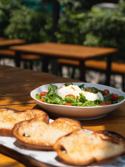 A plate of our fresh burrata salad with toasted sourdough bread, served in our sunny outdoor seating area.