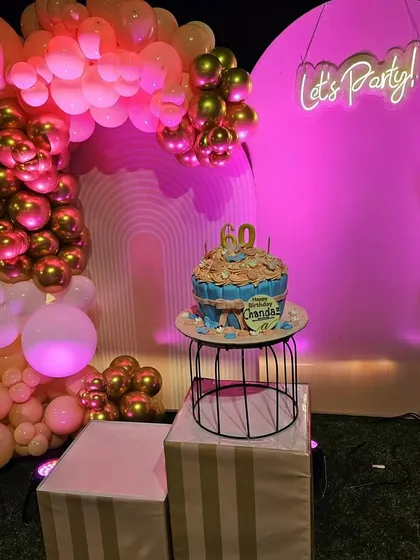 A wider view of the stylish 60th birthday party decor. The setup includes a beautiful balloon arch, neon signs, and a dedicated, well-lit area for the birthday cake, creating a perfect photo opportunity.