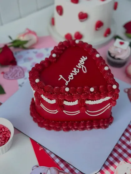 A classic vintage-style heart-shaped cake in vibrant red, with "Love you" written in elegant script.