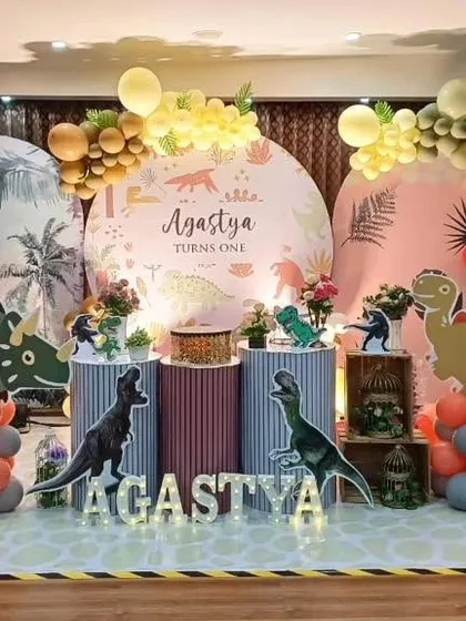 A large-scale dinosaur theme with multiple backdrops and realistic dinosaur props. The setup uses several pedestals for cake and dessert display.