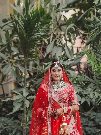 A stunning full-length bridal portrait, with the bride holding her kalire against a backdrop of lush greenery.