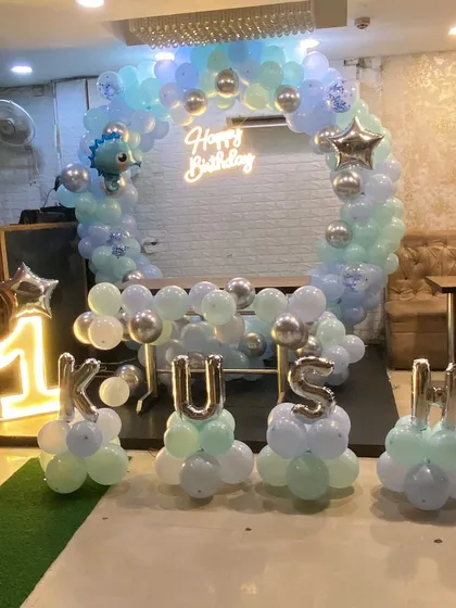 Celebrating a first birthday with a modern pastel theme. This decor features a half-arch of balloons, a 'Happy Birthday' neon sign, a light-up number '1' marquee, and the baby's name in silver foil balloons for a personalized touch.
