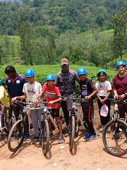 A group of young cyclists and their instructor pose for a photo amidst the scenic tea plantations of Barapole, Coorg.