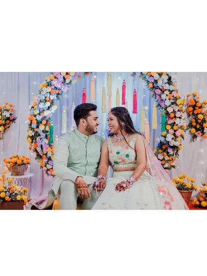 A classic portrait of the couple seated against their colourful Haldi decor.