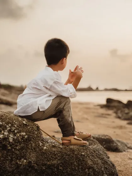 A boy sits on a rock, looking out at the ocean. This thoughtful, candid moment captures a different side of a kids outdoor photoshoot.