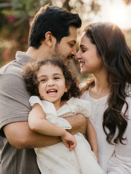 A family shares a laugh while the father holds their daughter. The warm backlighting and genuine joy make this a perfect candid family portrait.