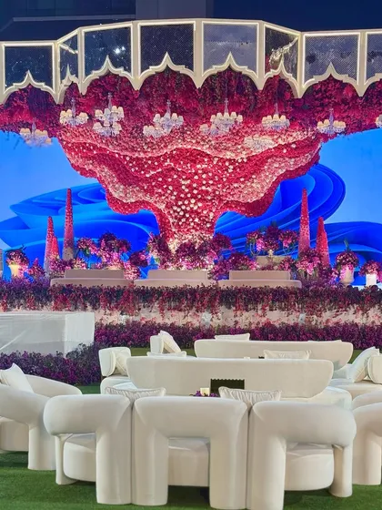For a celebration that demands drama and vibrancy, we craft scenes of unparalleled scale. This outdoor stage features a massive, sculptural floral canopy in bold reds and purples, set against a custom digital backdrop for a truly surreal experience. 💜