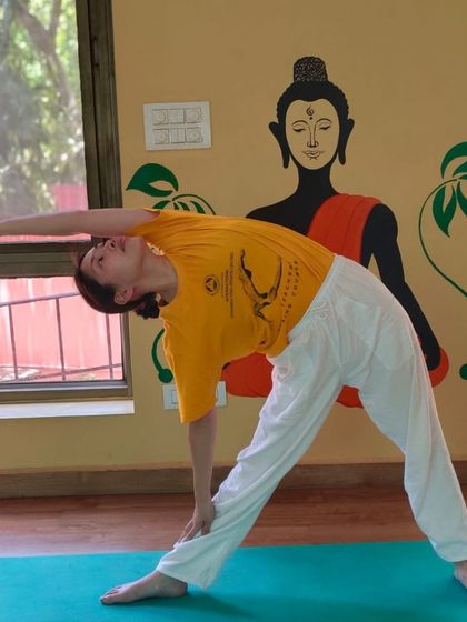 A student demonstrates Trikonasana (Triangle Pose) in front of a mural of the Buddha, reflecting the peaceful and mindful environment of our studio.