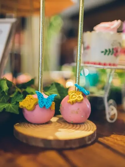 These delightful pink cake pops are decorated with tiny blue and yellow butterflies, adding a touch of delicate, edible art to the whimsical dessert table.
