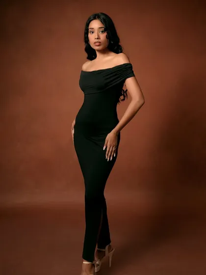 A full-length view of the elegant black dress against a warm brown background. This type of shot is essential for showing the complete look in a fashion catalog.