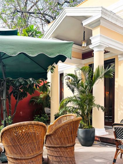 The beautiful, sunny exterior of a cafe with wicker chairs and lush plants, setting a perfect scene for a relaxed outing.