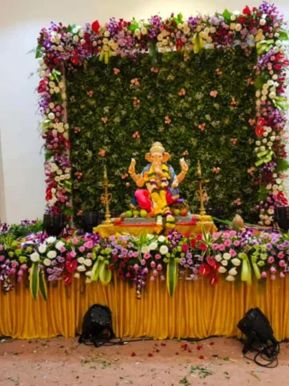 A large-scale Ganpati mandap for a society or public event, featuring a lush green backdrop framed with a wide variety of colorful fresh flowers. This design makes a grand statement.
